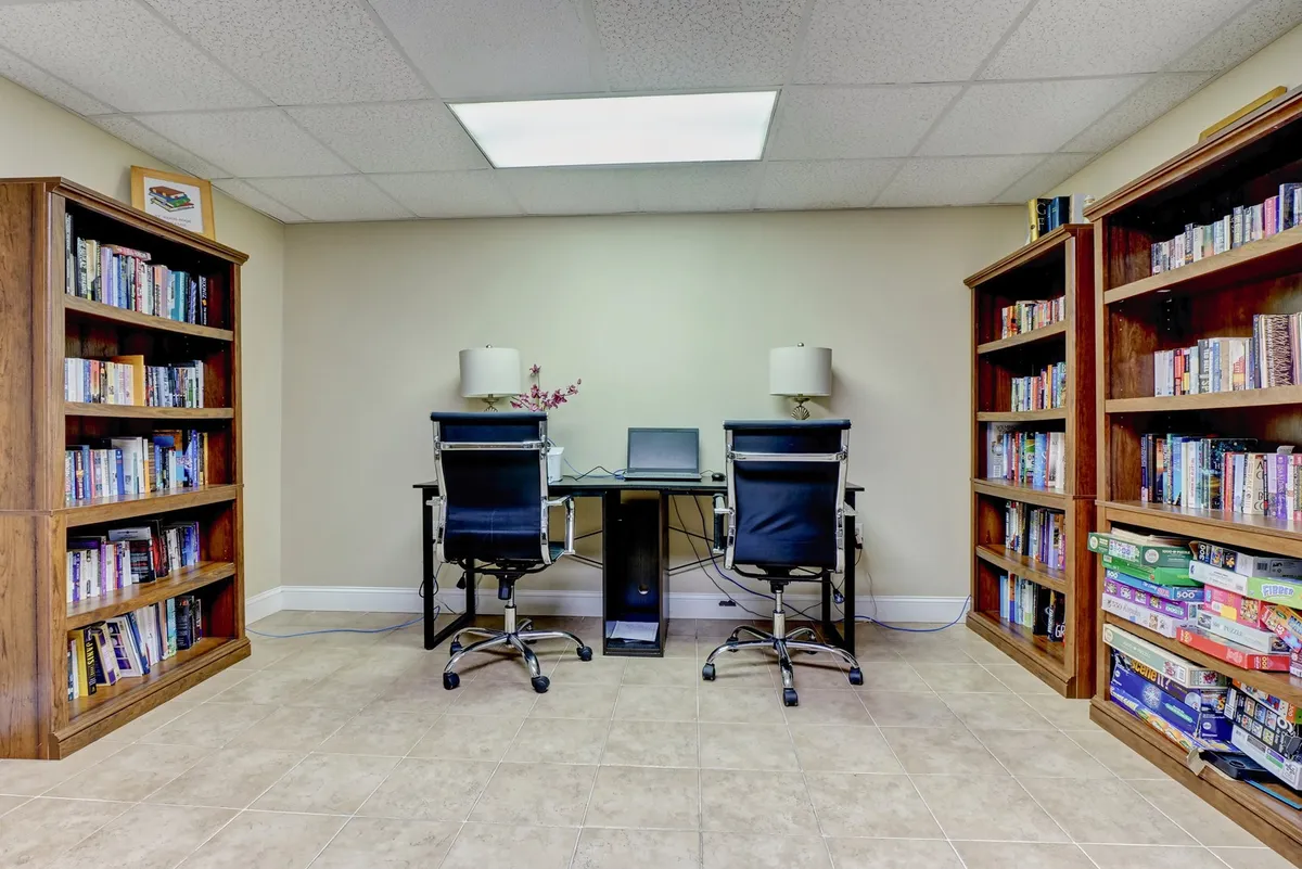 A cozy business center space featuring bookshelves filled with books, two desk chairs facing each other, and a small desk with a computer. The overall mood is intellectual and serene, making it ideal for remote work, reading, or collaborative activities.