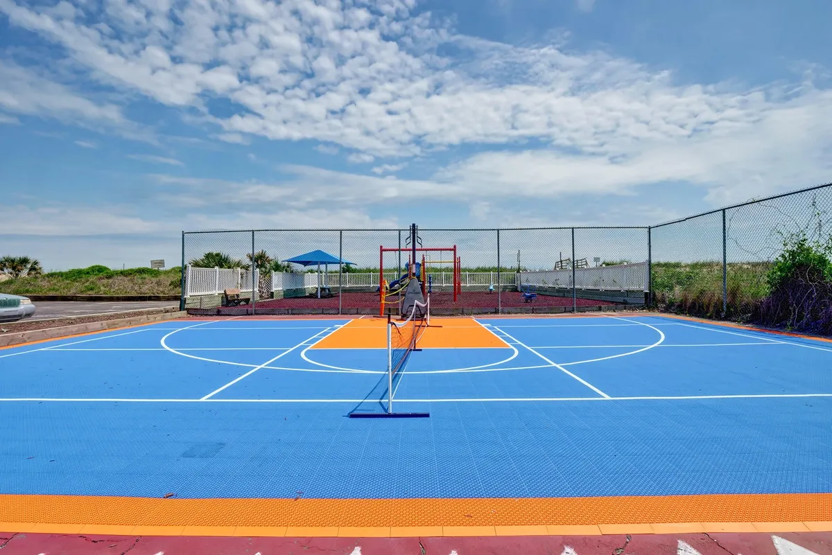 An outdoor sports area featuring a basketball court with a tennis net and a nearby play structure. The vibrant setting encourages energetic outdoor games, friendly competition, and playful family moments.