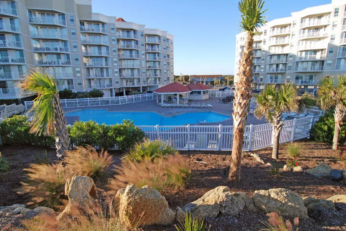 This image presents a sparkling swimming pool surrounded by palm trees and lounge areas, set against the backdrop of the building's architecture. The relaxed scene is inviting, with ample space for both swimming and sunbathing, and hints at family-friendly activities.