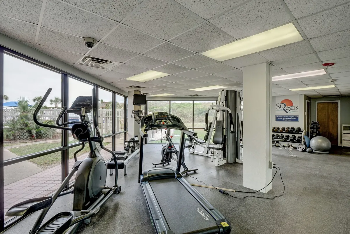 A bright, modern fitness center featuring a treadmill, elliptical machine, weight machines, and large windows that let in natural light. The scene is well-organized, motivating, and showcases the wellness-focused facilities available to guests.