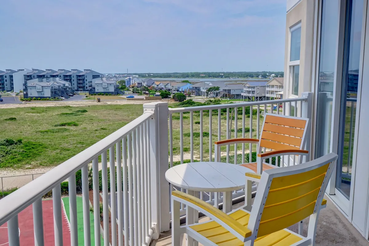 A private balcony scene with a yellow chair and white table, overlooking a sweeping view of the landscape and ocean horizon. The setting is inviting and intimate, perfect for morning coffee or watching the sunset together.
