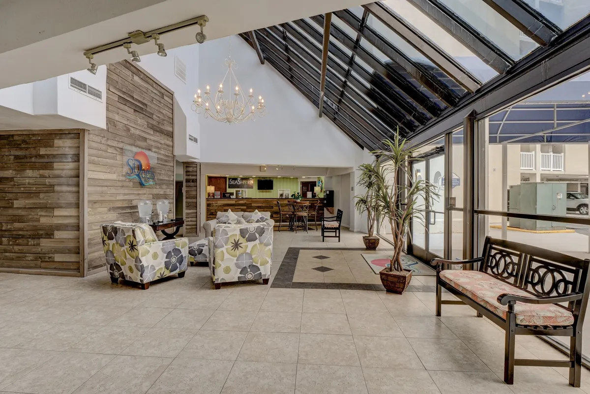 A welcoming reception area featuring a chandelier, a cozy seating area, and large windows that fill the space with natural light, creating an inviting first impression for guests arriving to work or explore.