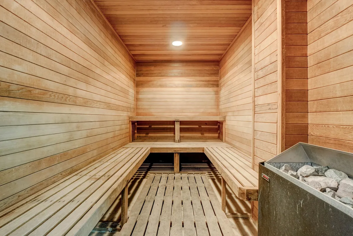 A tranquil sauna with wooden benches, a rock heater, and wood-paneled walls. The cozy, softly-lit space communicates relaxation, self-care, and opportunities for social wellness gatherings.